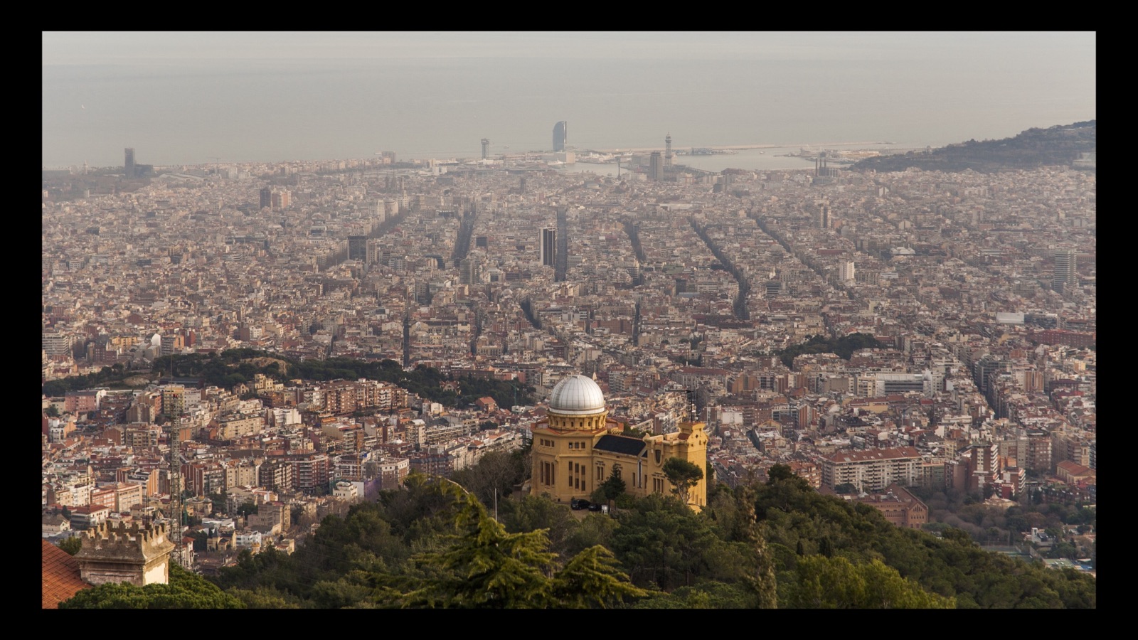 The Fabra Observatory's silver dome above Barcelona, with the city grid stretching to the harbour and the sea dissolving into haze