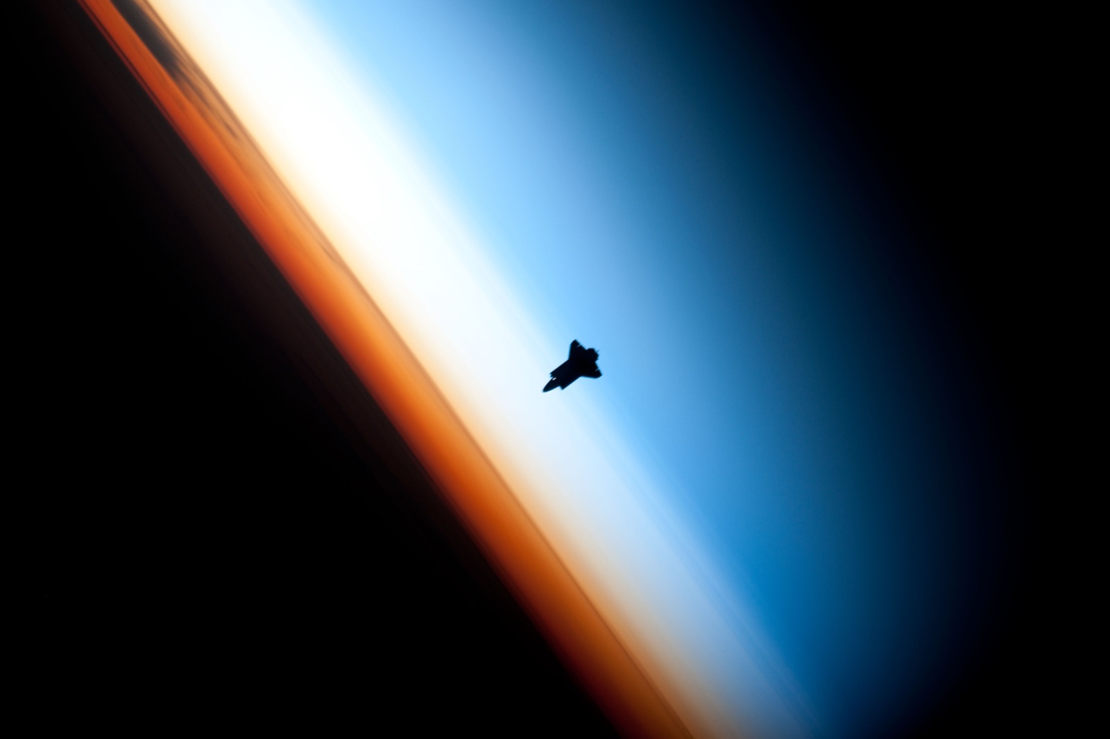 Silhouette of the space shuttle Endeavour against Earth's thin blue atmospheric limb, photographed from the ISS