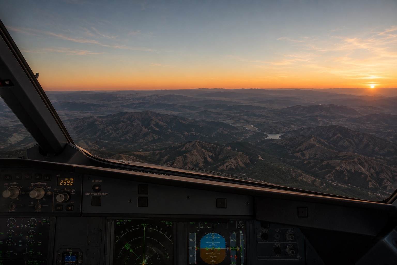 Cockpit view at cruising altitude: mountain ridgelines stretching to a sunset horizon beyond the instrument panel