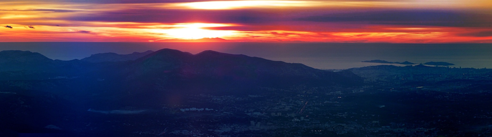 Sunset panorama from Pic de Bertagne in Provence: the sun dropping behind the silhouette of Canigou on the horizon 278 km away, with Marseille's coastline below