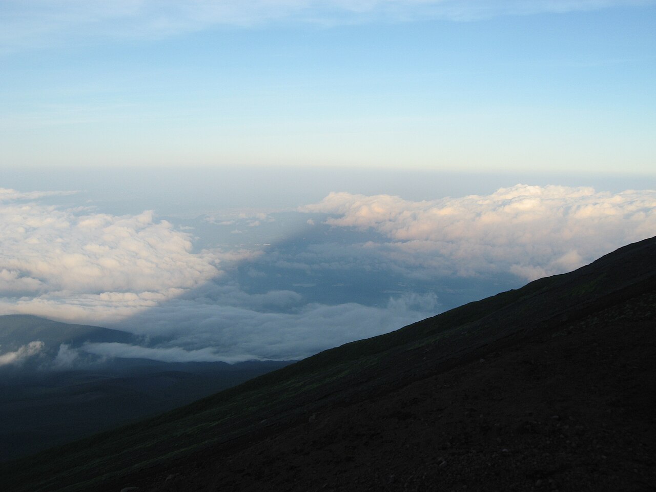 The shadow of Mount Fuji cast over a sea of clouds at dawn, seen from the mountain's slope