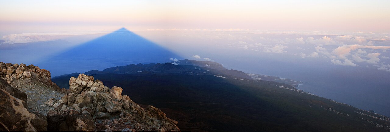 Panoramic view from Teide's summit at dawn with the triangular shadow stretching over the island's coast and the sea
